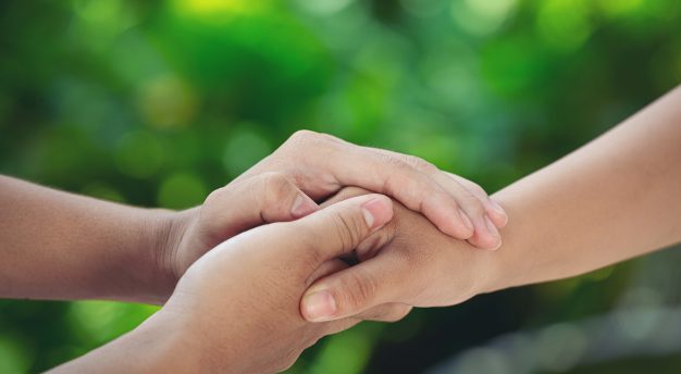 Couple holding hands in green meadow.